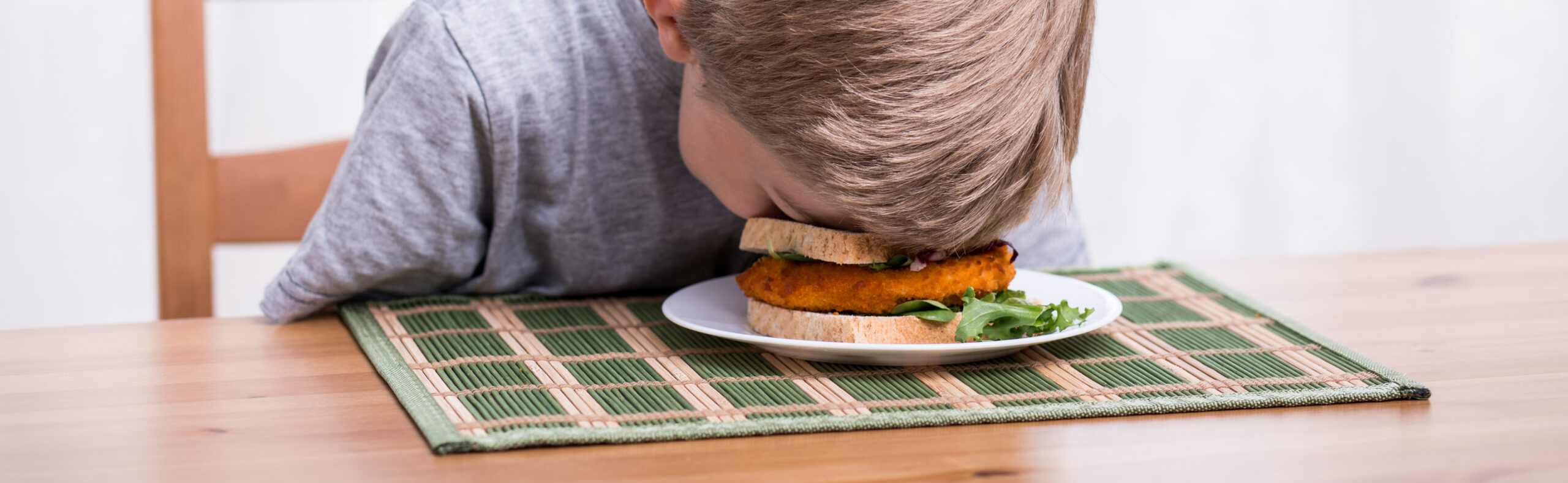 boy with face in sandwich at table